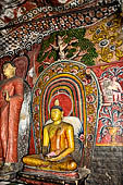 Dambulla cave temples - the narrow Cave 1, Devaraja Viharaya (Temple of the Lord of the Gods) statue of Ananda at the feet of the sleeping Buddha statue. 