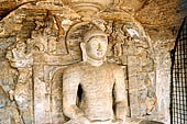Polonnaruwa - Gal Vihara. The small seated Buddha (x century), kept behind a metal grille and placed in a recess of the rock with in the background a torana and attendant deities.