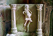 Il complesso parrocchiale, enclos, di La Martyre. Acquasantiera all'interno del portico meridionale della chiesa di San Salomone. Raffigurazione della morte, l'ankou, con una testa decapitata. 