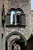 Randazzo - via degli Archi, arches in black pumice stone with a double lancet window and a white twisted column. 