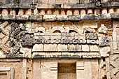 Uxmal - The Nunnery Quadrangle, the North Building. Detail of the frieze between the first and the second masks stack: traditional hut surmounted by three double-headed serpents.  