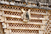 Uxmal - The Nunnery Quadrangle. The Eastern building. Frieze showing trapezoidal tiering of 8 double headed serpents bars, with small owl head at top against a latticework background. 
